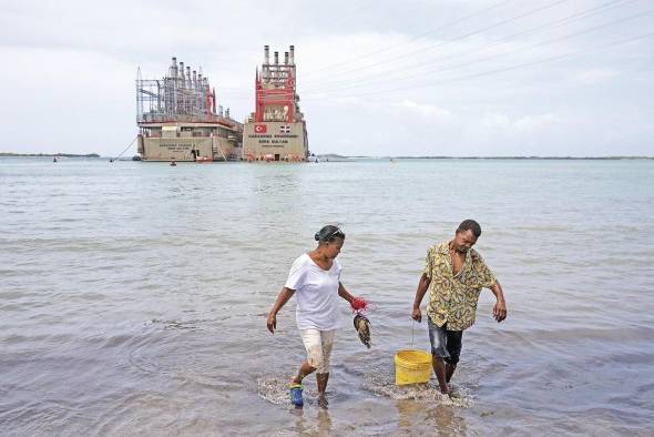 Trabajadores lavan pescados en la costa cerca de las dos barcazas de generación de energía eléctrica. Trabajadores lavan pescados en la costa cerca de las dos barcazas de generación de energía eléctrica.