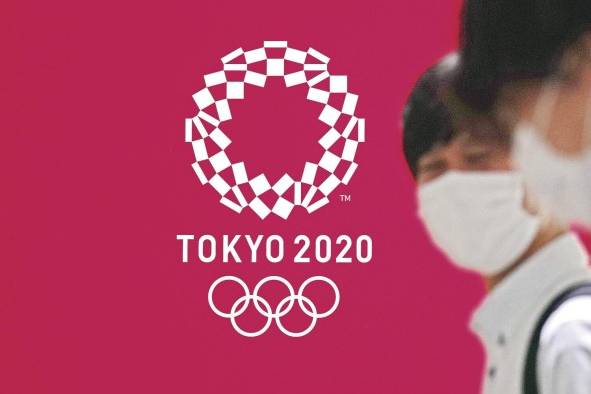 Fotografía de archivo de personas con tapabocas pasando frente a un cartel con la imagen de los Juegos Olímpicos Tokio 2020. Fotografía de archivo de personas con tapabocas pasando frente a un cartel con la imagen de los Juegos Olímpicos Tokio 2020.