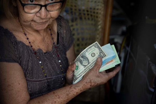 Una mujer sostiene dólares y bolívares en una tienda. | Una mujer sostiene dólares y bolívares en una tienda. |
