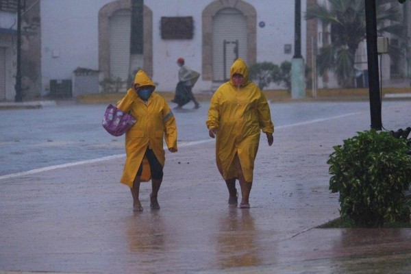 Dos personas protegidas con capas caminan en medio de un fuerte aguacero en el estado de Yucatán (México). Dos personas protegidas con capas caminan en medio de un fuerte aguacero en el estado de Yucatán (México).