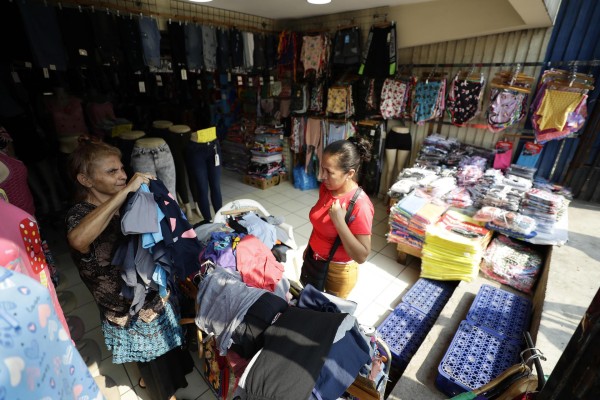 Una mujer muestra prendas de vestir a una clienta en una tienda de ropa, el 18 de abril de 2023, en el centro de San Salvador Una mujer muestra prendas de vestir a una clienta en una tienda de ropa, el 18 de abril de 2023, en el centro de San Salvador