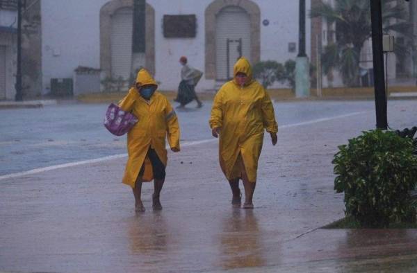 Dos personas protegidas con capas caminan en medio de un fuerte aguacero en el estado de Yucatán (México). Dos personas protegidas con capas caminan en medio de un fuerte aguacero en el estado de Yucatán (México).
