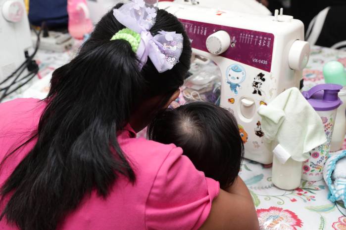Una niña realiza un vestido mientras sostiene a su hijo en brazos. Una niña realiza un vestido mientras sostiene a su hijo en brazos.