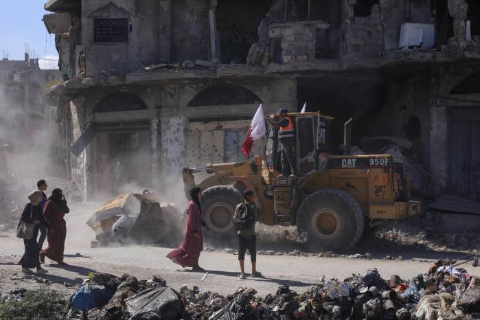 Palestinos caminan junto a una excavadora desplegada por la Municipalidad de Gaza para limpiar los escombros de los edificios. Palestinos caminan junto a una excavadora desplegada por la Municipalidad de Gaza para limpiar los escombros de los edificios.