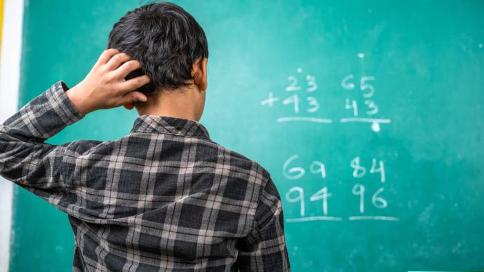 Confused kid scratching head to solve mathematics problem on board at classroom - concept of intelligence, trouble learning and education Confused kid scratching head to solve mathematics problem on board at classroom - concept of intelligence, trouble learning and education