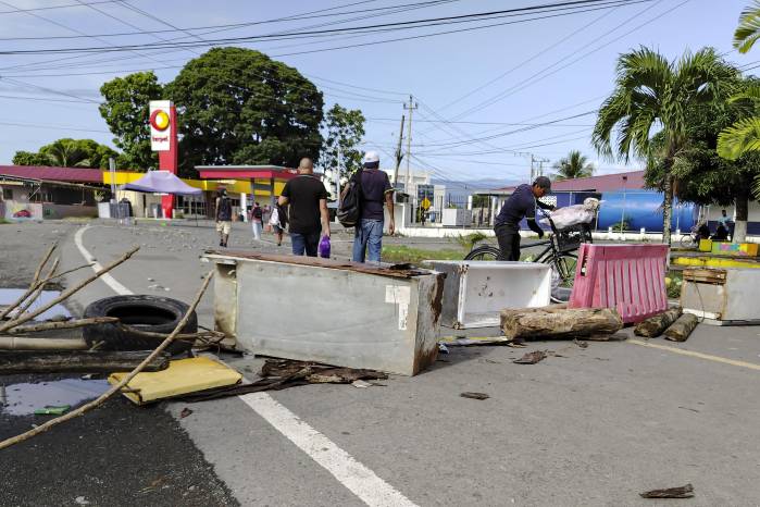Personas caminan junto a una barricada en la vía en Changuinola luego de que grupos de vándalos irrumpieran en el aeropuerto local. Personas caminan junto a una barricada en la vía en Changuinola luego de que grupos de vándalos irrumpieran en el aeropuerto local.