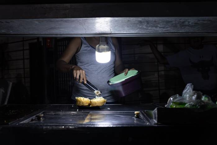 Una persona vende comida ayudada con un bombillo en medio de la oscuridad, durante un corte eléctrico, el 29 de febrero de 2024 en Maracaibo (Venezuela). Una persona vende comida ayudada con un bombillo en medio de la oscuridad, durante un corte eléctrico, el 29 de febrero de 2024 en Maracaibo (Venezuela).