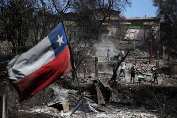 Una bandera chilena ondea mientras los vecinos limpian sus tierras y queman casas en Villa Independencia, región de Valparaíso, Chile.