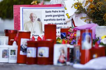 Los fieles dejan velas y tarjetas a los pies de la estatua de Juan Pablo II en la entrada del Hospital Gemelli, donde está hospitalizado el Papa Francisco.