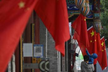 Un niño toca una bandera china colgada en una calle de Beijing, en China.