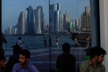 Personas se sientan con el reflejo del horizonte de Doha a lo largo de la Corniche de Doha.