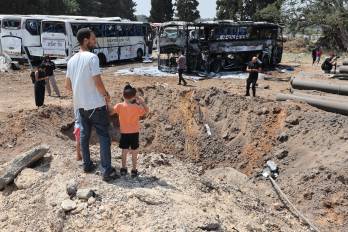 Personas se encuentran frente a un enorme cráter en el lugar del impacto de un misil iraní en una estación de autobuses en Herzliya.