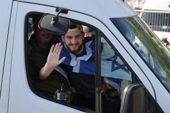 Bar Kuperstein, one of the released Israeli hostages formerly held captive in Gaza since the 2023 October 7 attacks by Palestinian militants, waves from the window of a bus at Sheba Tel-HaShomer Medical Centre in Ramat Gan on October 13, 2025. (Photo by AHMAD GHARABLI / AFP)