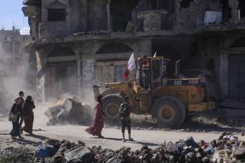 Palestinos caminan junto a una excavadora desplegada por la Municipalidad de Gaza para limpiar los escombros de los edificios.