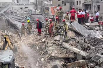 Miembros de la Media Luna Roja Iraní y bomberos iraníes buscando entre los escombros de un edificio derrumbado tras un presunto ataque militar.