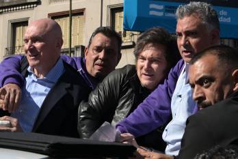 Milei (centro) reacciona junto al candidato a diputado del partido gobernante, José Luis Espert (izq.), y personal de seguridad, mientras manifestantes les lanzan objetos durante una caravana en Lomas de Zamora.