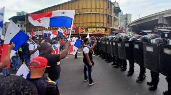 Manifestantes portan banderas frente a la unidad antidisturbios apostada frente a la plaza 5 de Mayo, durante la visita de Pete Hegseth.