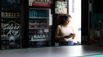 Una mujer que observa un teléfono celular fue captada este miércoles, 16 de abril, en la puerta de una tienda, durante un apagón eléctrico, en San Juan.