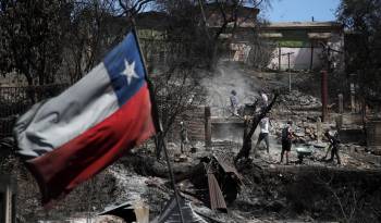 Una bandera chilena ondea mientras los vecinos limpian sus tierras y queman casas en Villa Independencia, región de Valparaíso, Chile.
