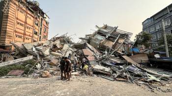 Personas permanecen junto a los escombros de un edificio derrumbado en Mandalay después del terremoto.