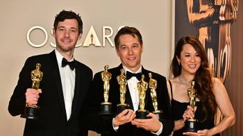 El productor estadounidense Alex Coco (izq.) y la productora estadounidense Samantha Quan (der.) posan con sus premios a Mejor Película por “Anora” junto al cineasta estadounidense Sean Baker.
