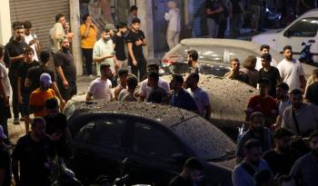 Los transeúntes rodean vehículos cubiertos de escombros cerca del lugar de un ataque militar israelí en los suburbios del sur de Beirut el 30 de julio de 2024.