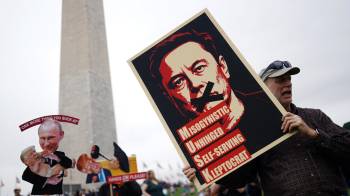 Un manifestante sostiene un cartel que representa a Elon Musk con el texto '¡Manos afuera!' en el National Mall en Washington, DC.