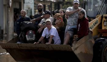 Personas son transportadas en una retroexcavadora luego de ser rescatadas en el barrio Sarandí en Porto Alegre.
