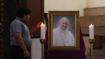 Una persona enciende una vela frente a un retrato del papa Francisco.
