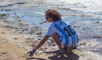 Una mujer vistiendo la camiseta del astro argentino del fútbol Lionel Messi, mientras recoge botellas de plástico del río Paraná en Rosario , Argentina.