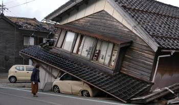 Una mujer observa una vivienda y vehículos dañados tras un fuerte terremoto en Tohi Town, en la península de Noto, Japón, este 2 de enero de 2024.