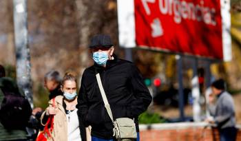 Fotografía de archivo de personas con mascarillas caminando en el entorno de un centro sanitario.