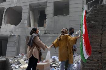 Dos hermanas iraníes se dan la mano frente a un edificio dañado en el sur de Teherán, Irán, el 15 de marzo de 2026.