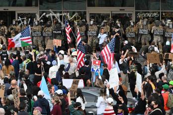 La Guardia Nacional de California y la Oficina de Aduanas y Protección Fronteriza de EE. UU. observan a los manifestantes congregados frente al Edificio Federal antes de la entrada en vigor del toque de queda.