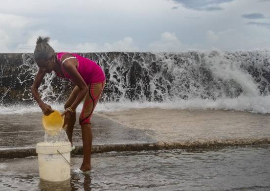 Una mujer posa mientras recoge agua de mar para limpiar su casa, en el malecón de La Habana
