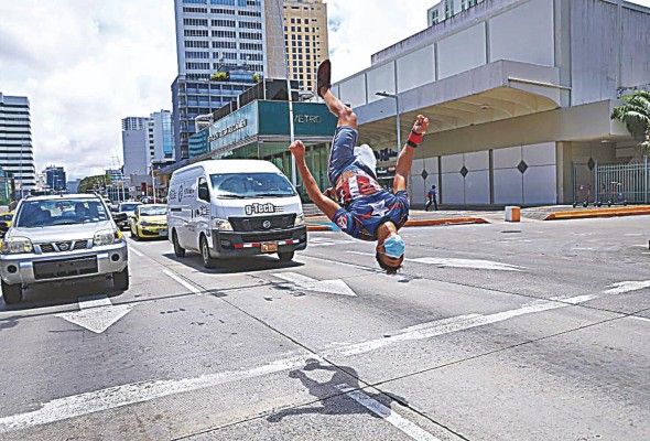 El deportista Fernando Diaz, especializado en gimnasia artística y 'parkour', desarrolla sus rutinas frente a la estación del metro Iglesia del Carmen, en busca de salir adelante con un sustento económico.