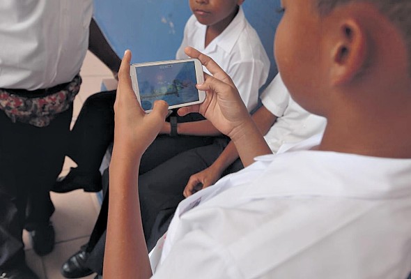 En la imagen se observa a un estudiante con una aparato móvil, un medio tecnológico muy utilizado durante la pandemia para recibir educación.