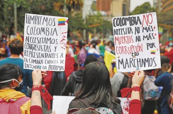 Una mujer sostiene dos carteles durante una movilización para rechazar la violencia ocurrida en las protestas del 6 de mayo en el Parque Nacional de Bogotá.