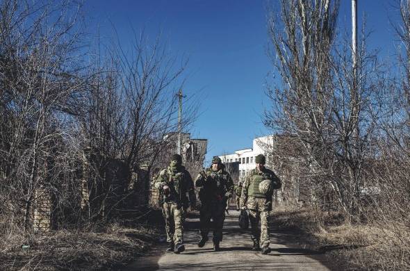 Varios soldados ucranianos caminan frente a unas ruinas en un pueblo cercano a la línea de contacto