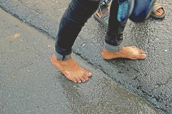 Manuel Rivera, un migrante de 19 años, camina descalzo para no mojar sus zapatos por la lluvia.