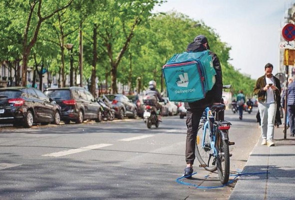 Un ciclista con una bolsa de la empresa 'Deliveroo' se detiene en una calle de París, en una imagen de archivo.