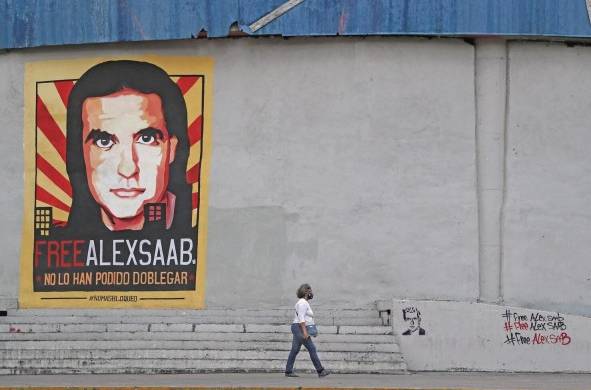 Una mujer pasa frente a un cartel y mensajes de apoyo al empresario colombo-venezolano Alex Saab en Caracas (Venezuela)