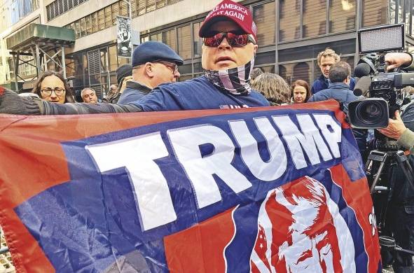 Dion Cini, quien organizó por redes sociales la marcha de “regreso a casa” para Trump, sostiene una bandera con la imagen del exmandatario.