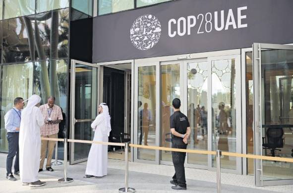 La gente espera afuera de un edificio decorado con el logotipo de la COP28 antes de la cumbre climática en Dubai.
