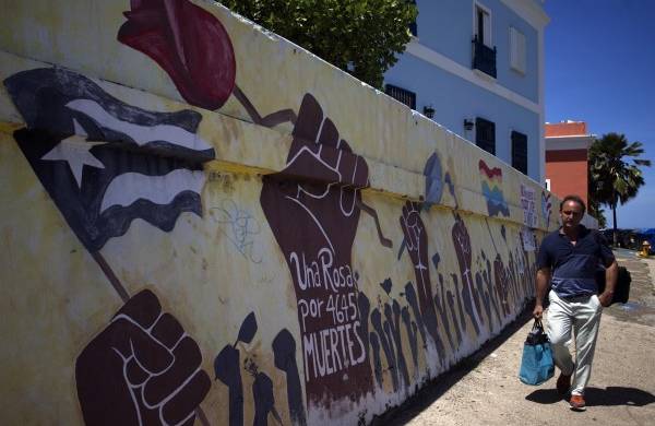 Fotografía del 13 de septiembre de 2022 donde aparece un hombre mientras camina frente a un mural que recuerda a los 4645 muertes provocadas por el paso en el 2017 del huracán María por San Juan, Puerto Rico.