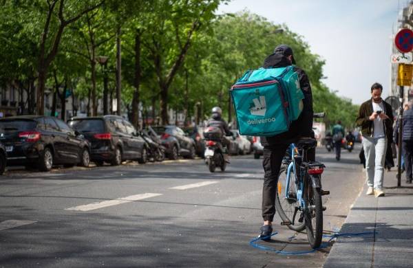 Un ciclista con una bolsa de la empresa 'Deliveroo' se detiene en una calle de París, en una imagen de archivo.