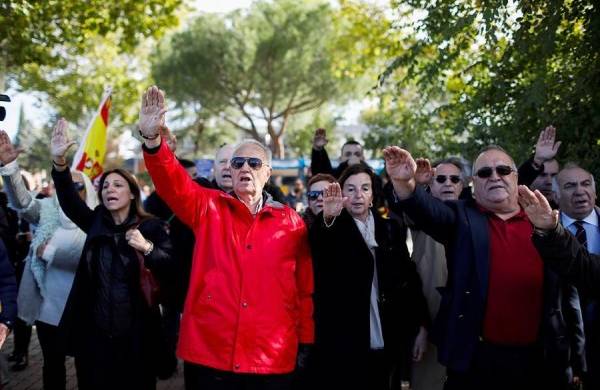 Un grupo de personas se concentran en el acceso del cementerio de El Pardo-Mingorrubio donde será llevado Franco al tiempo que hacen el saludo fascista.