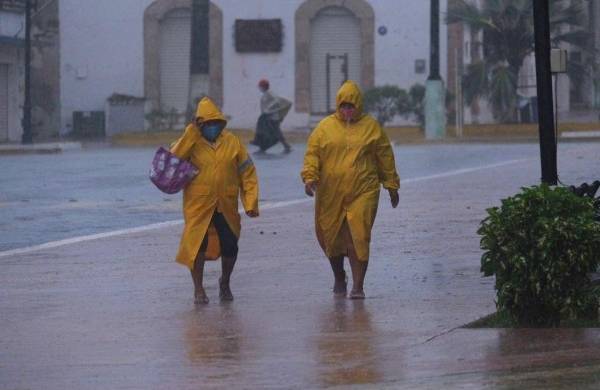 Dos personas protegidas con capas caminan en medio de un fuerte aguacero en el estado de Yucatán (México).
