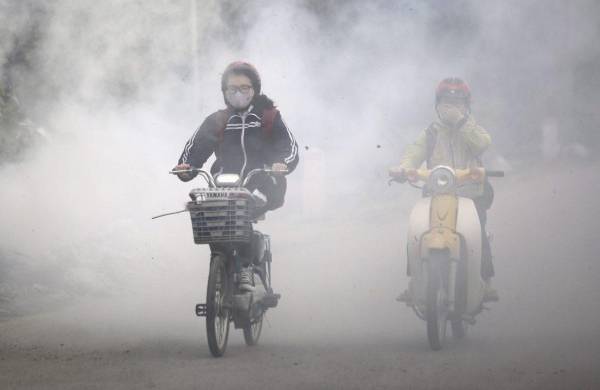 En la imagen de archivo, varias personas circulan entre el humo generado por residuos quemados en las calles de Hanoi, Vietnam.