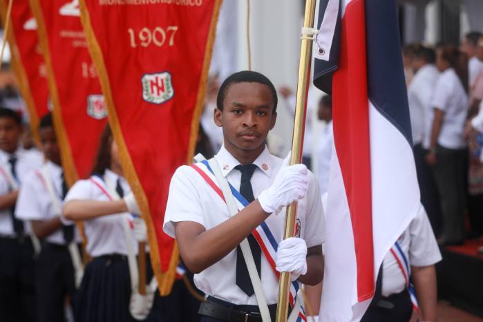 Jóvenes abanderados marchan con orgullo portando el tricolor nacional frente al Palacio de las Garzas.